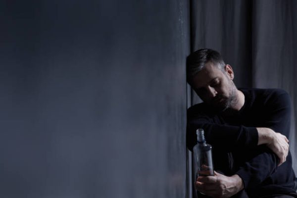 Man holding bottle of alcohol in dark interior Man holding bottle of alcohol in dark interior